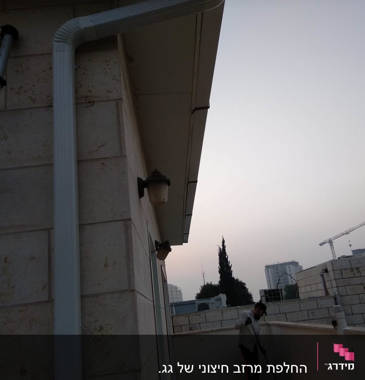 מרזב לבן מחובר לגג בניין אבן